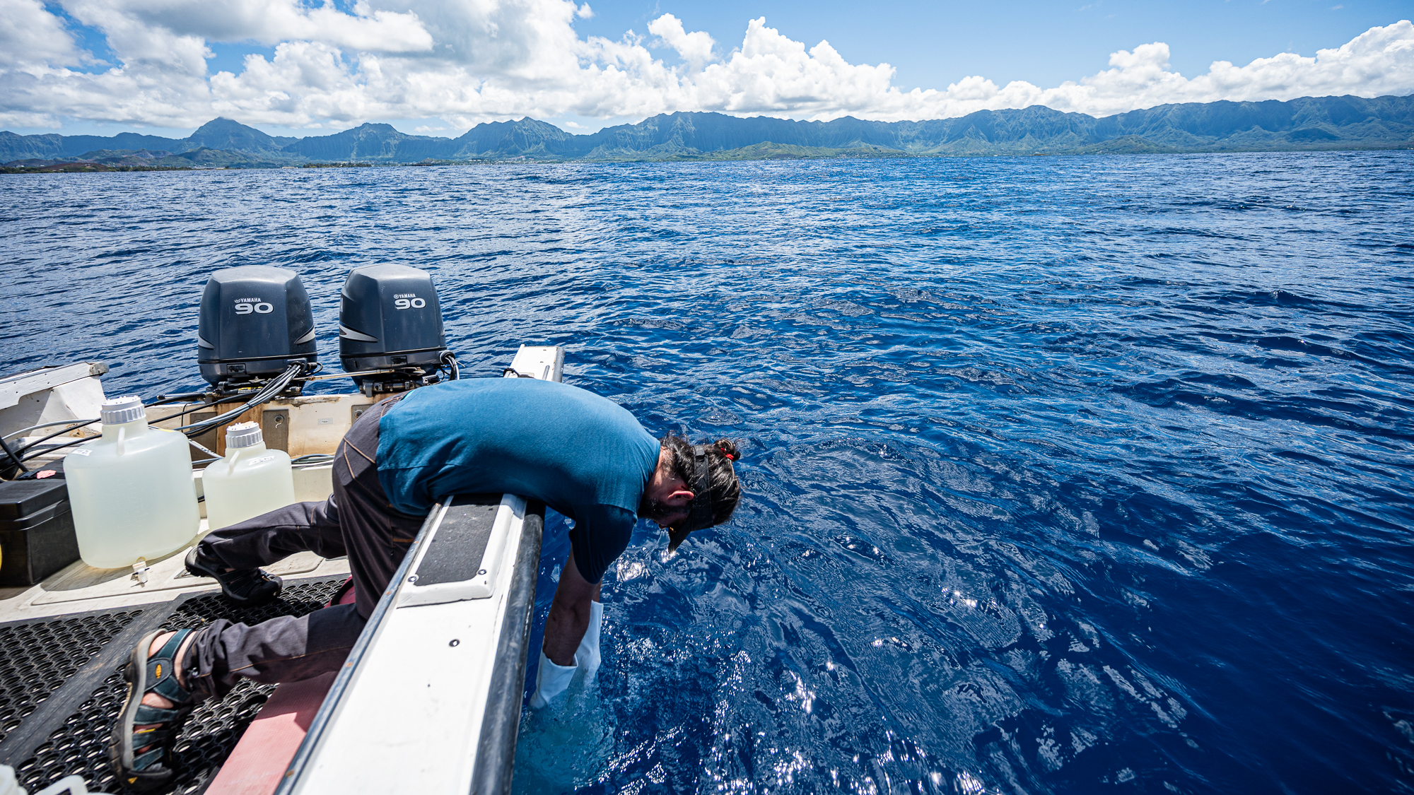 A photo of Meren collecting seawater from the side of a small boat.