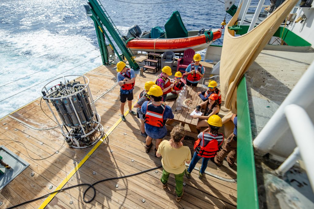 A group of researchers stand on the deck of a ship next to a CTD rosette.